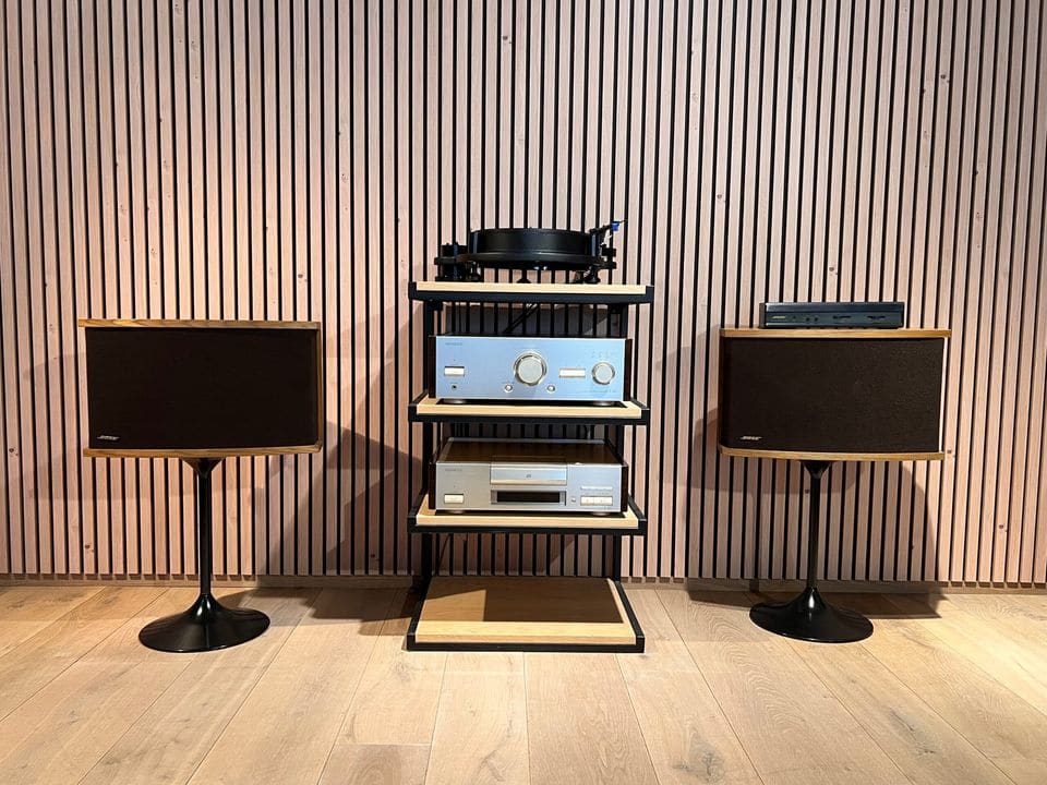 Paar Bose 901 Series VI luidsprekers op tulpvoeten naast een hifi-rack, met frontdoek