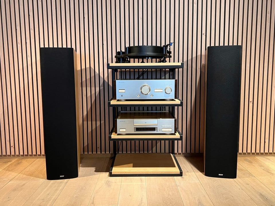 Paar B&W DM 604 S3 vloerstaande luidsprekers met zwart frontdoek naast een hifi-rack