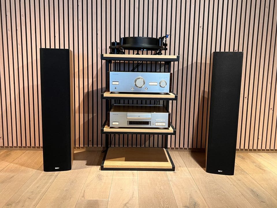 Paar B&W DM603 S3 vloerstaande luidsprekers met zwarte frontdoeken naast een hifi-rek