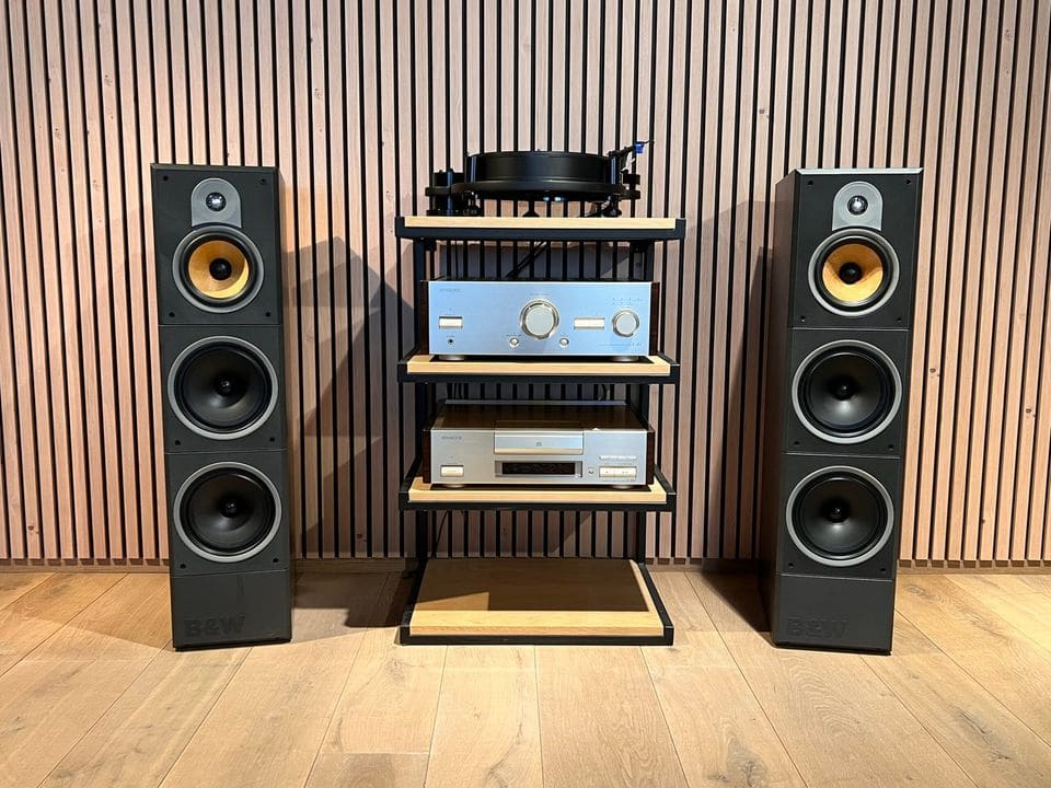 Paar zwarte B&W DM640i vloerstaanders zonder frontdoek naast een hifi-rek