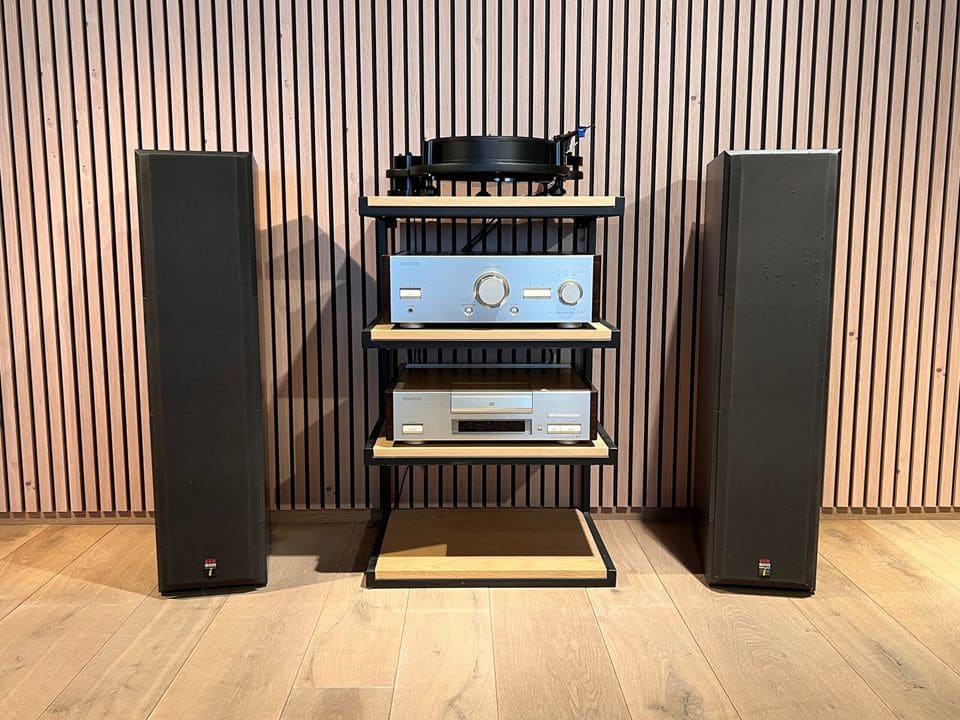Paar B&W DM640i luidsprekers met zwarte frontdoeken naast een hifi-rek