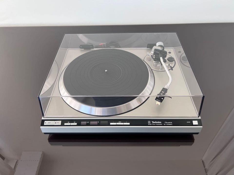 Technics SL-1400 MK2 zilveren platenspeler met gesloten stofkap, vooraanzicht op een donkere tafel