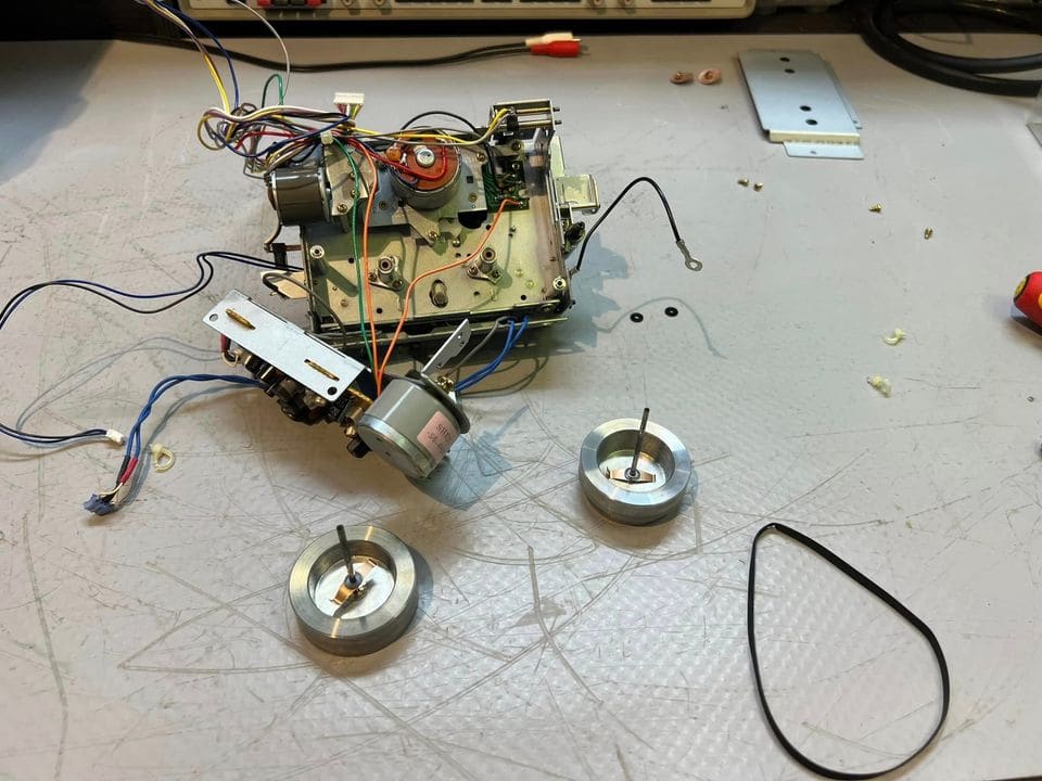 Gedemonteerd DR-2-mechanisme met de twee capstanvliegwielen, een motor en een aandrijfriem los op de werkbank