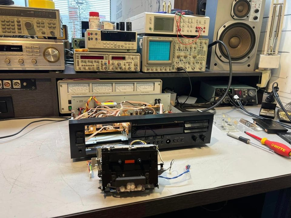 Geopende Nakamichi DR-2 met het uitgebouwde cassettemechanisme ervoor op de werkbank